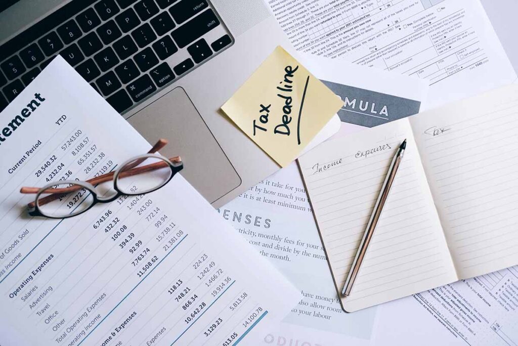 Paperwork and Laptop on Desk with Tax Deadline Stick Note